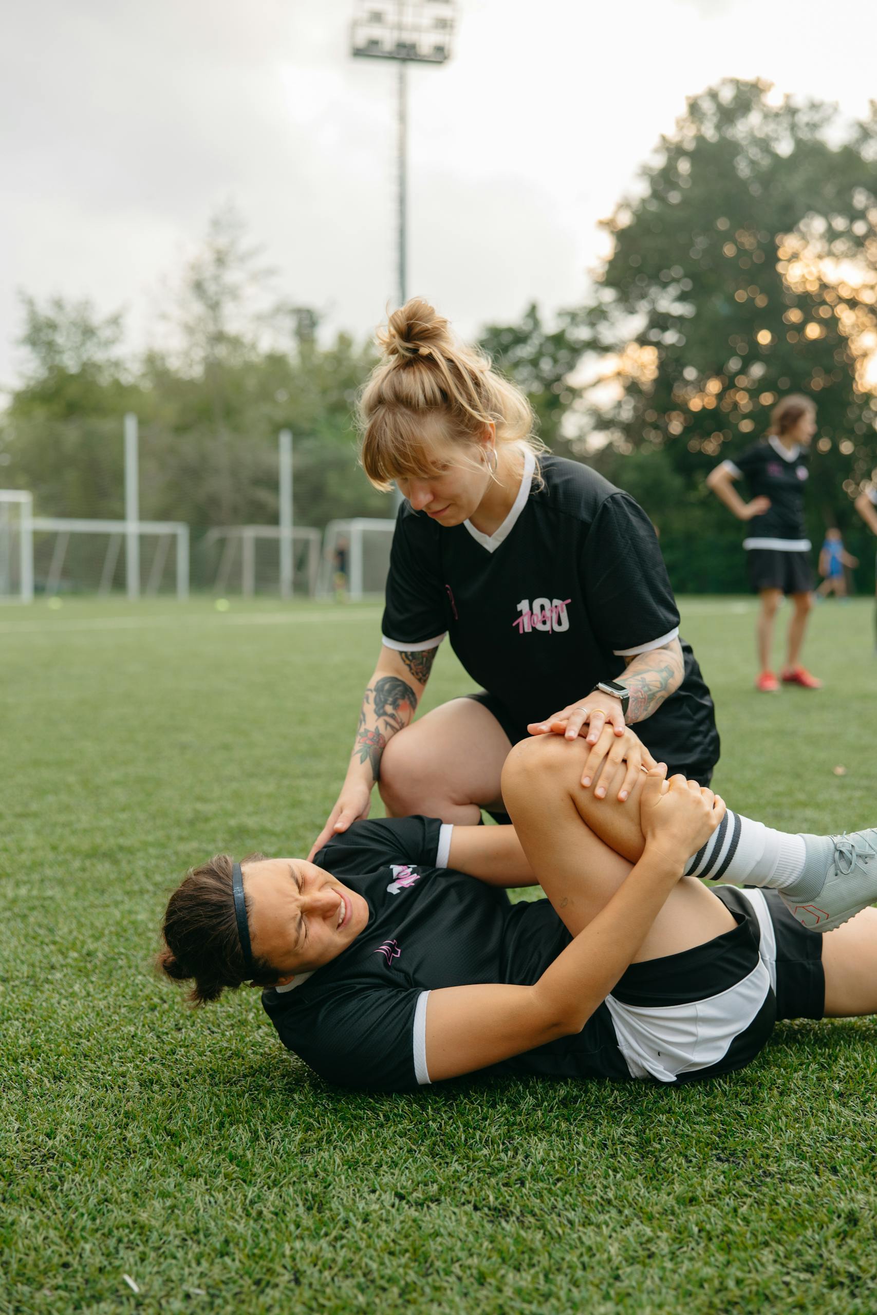 A female soccer player helps her injured teammate during a practice session on a soccer field.